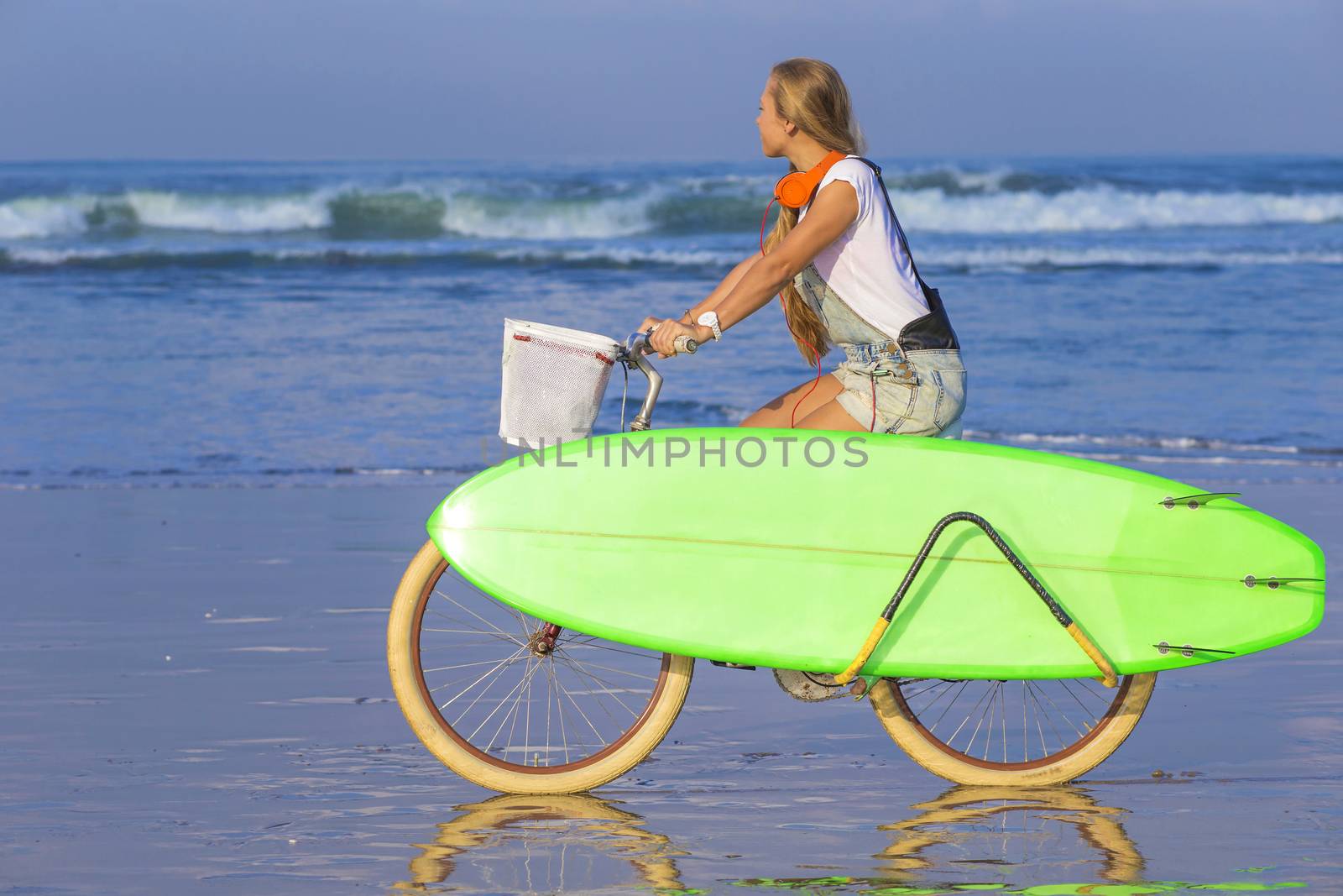 Young girl with surfboard and bicycle on the beach.