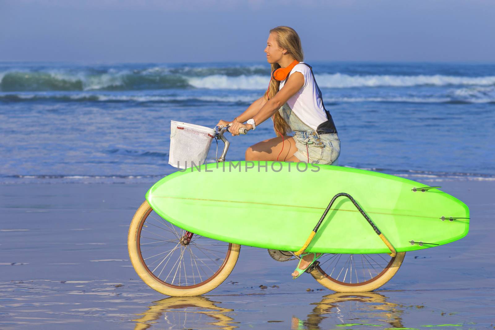 Young girl with surfboard and bicycle on the beach.