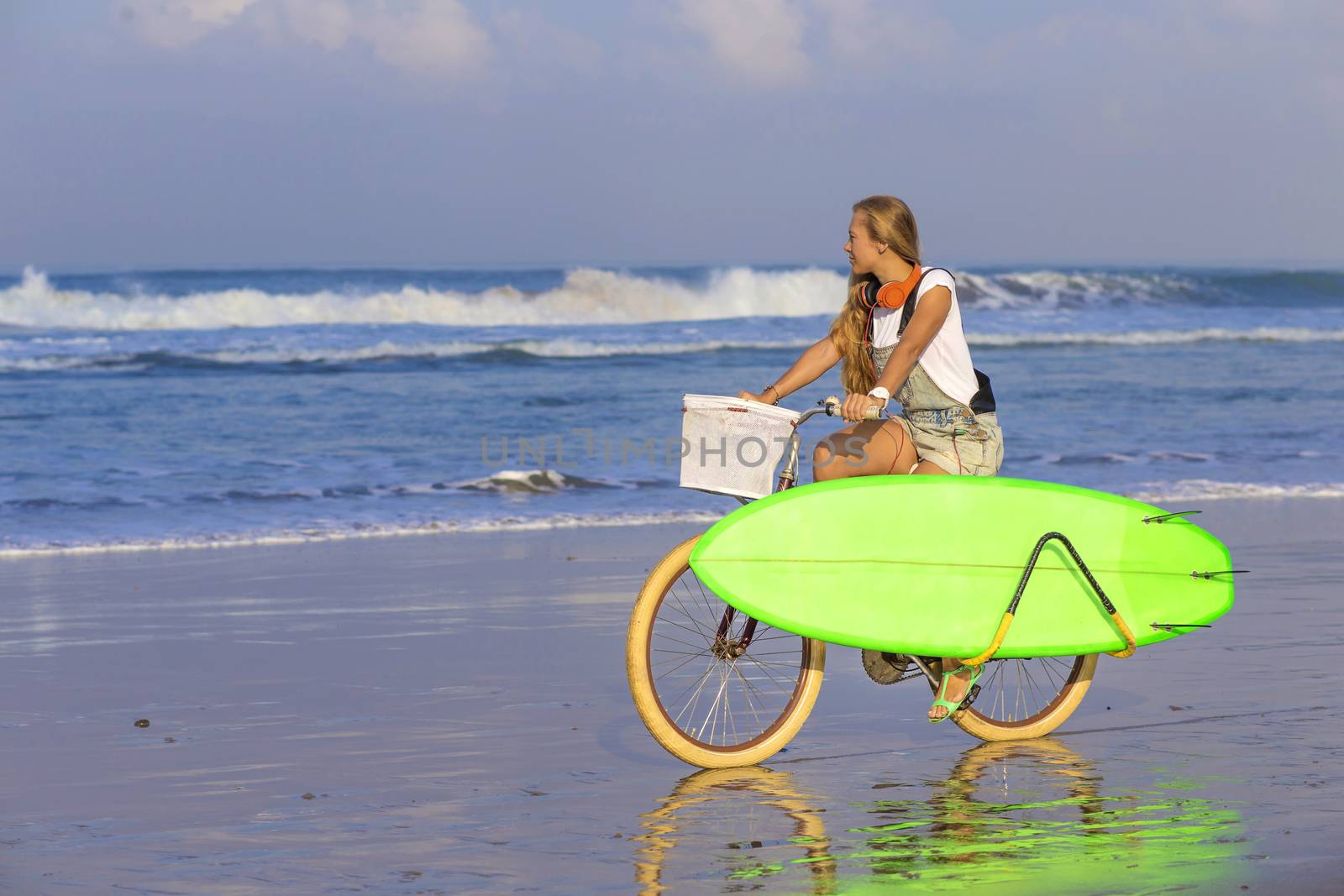 Young girl with surfboard and bicycle on the beach.