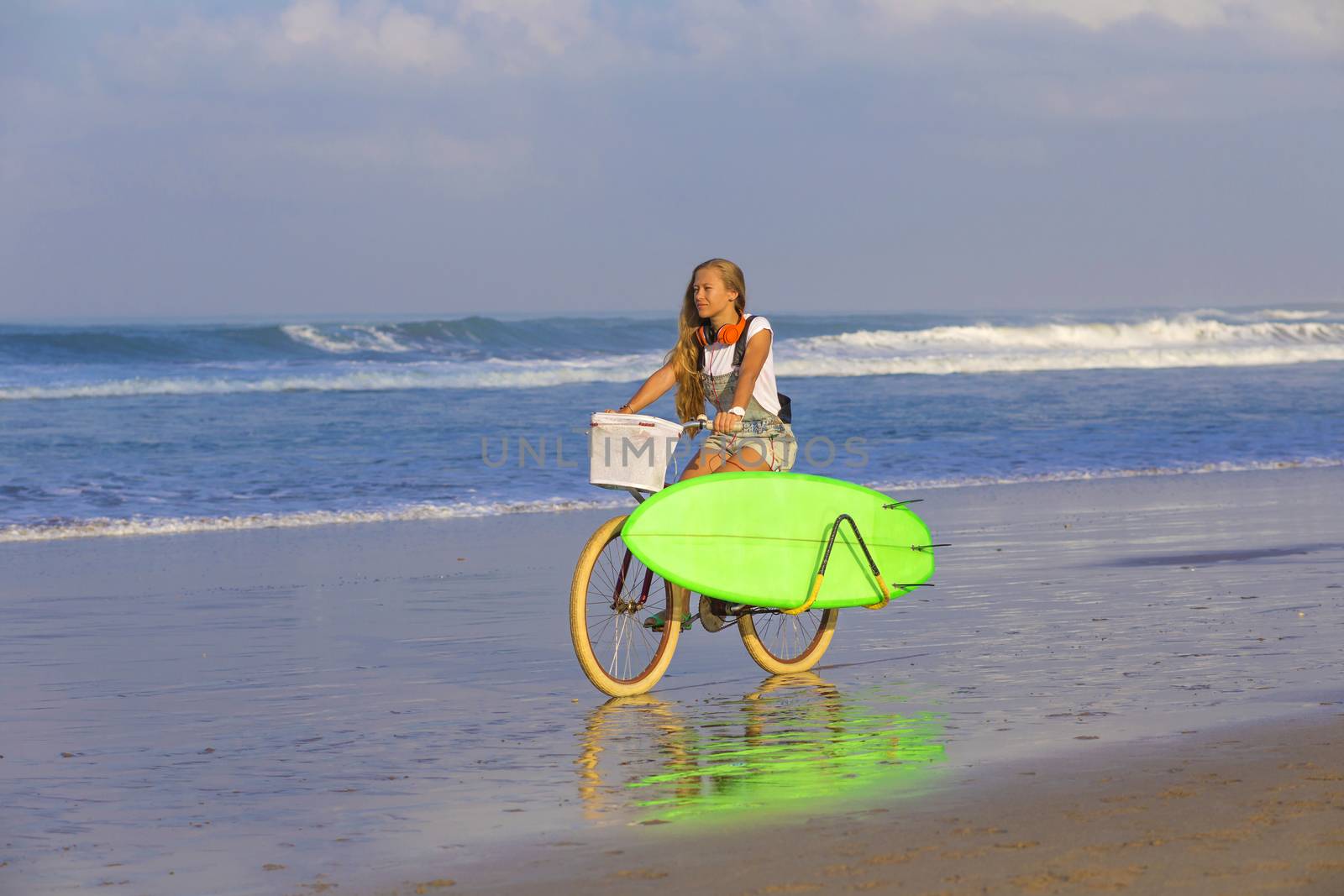 Young girl with surfboard and bicycle on the beach.