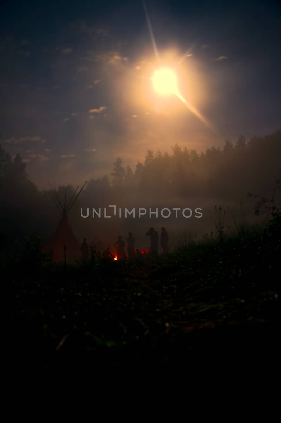 Group standing around campfire in mystical darkness lit by moonlight