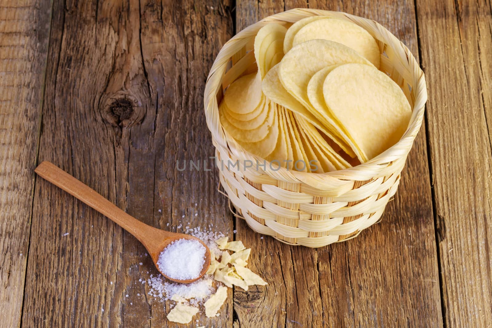 potato chips in a wooden basket and spoon on wooden table