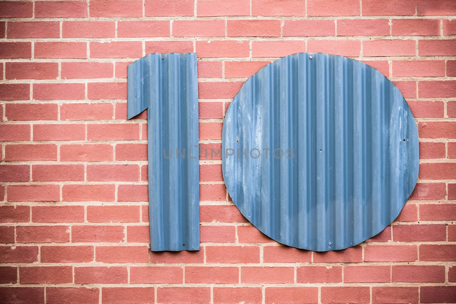 The number ten cut out of corrugated iron and placed on a face brick wall.