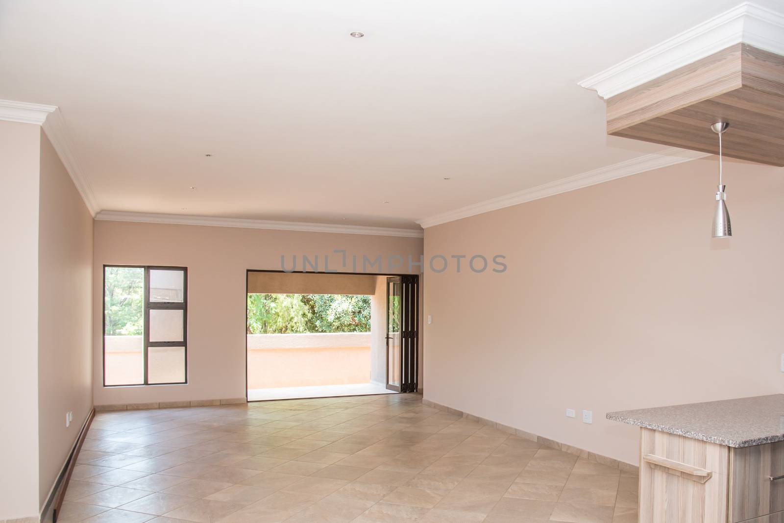 A view of the living room of a newly build and vacant house looking from the kitchen, through the living area, towards the patio.