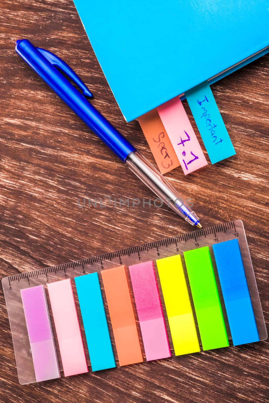 Multi coloured page markers on a table with a pen and a book of which three pages has already been marked.