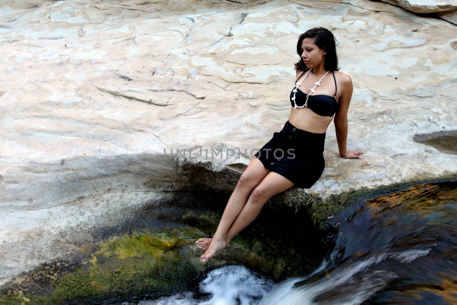 Hispanic woman with bikini sitting next to a waterfall.