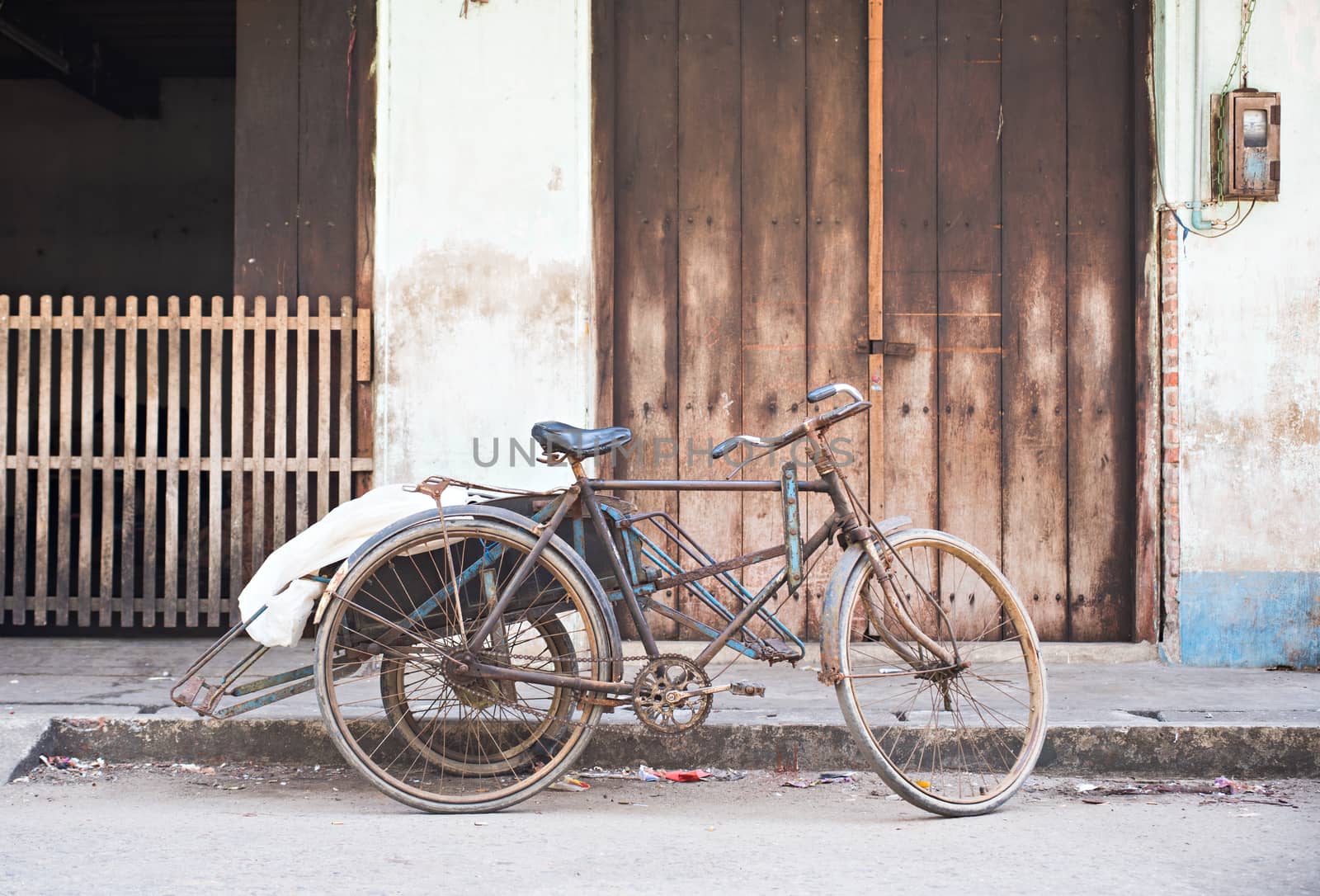 Old, rusty cyclo in front of a warehouse at a street in Myeik, Myanmar.