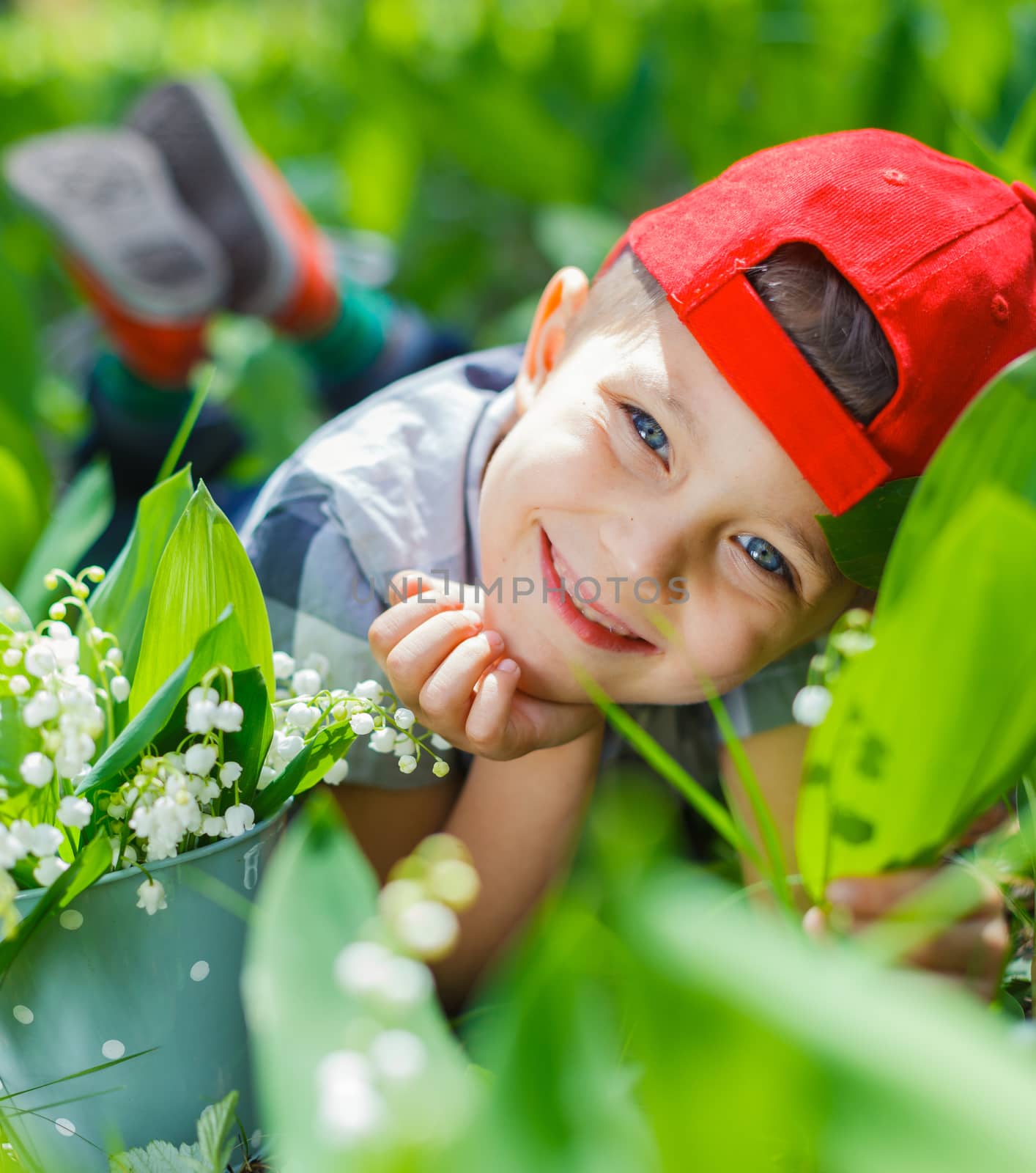 Cute little boy with lilies of the valley in forest on spring day