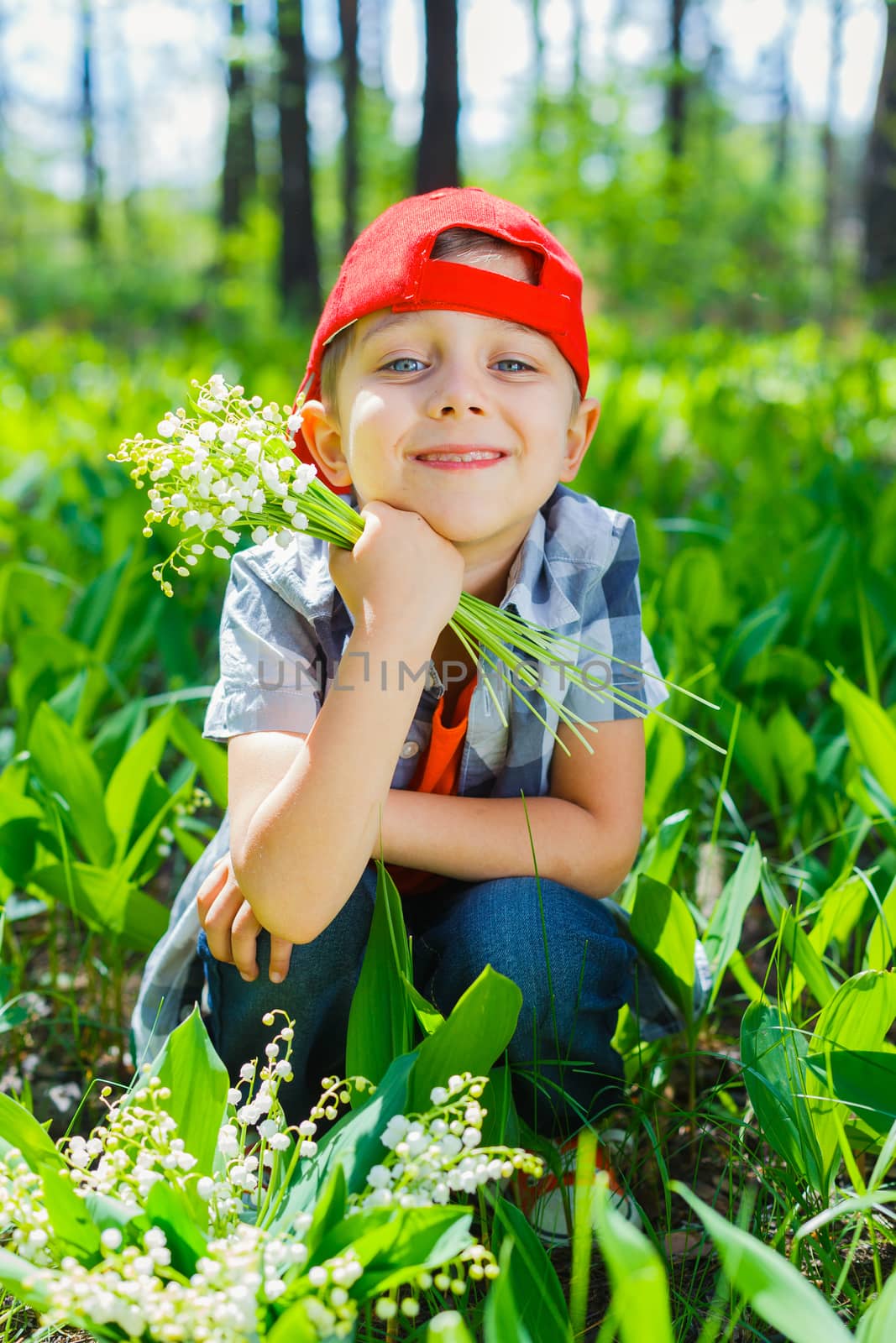 Cute little boy with lilies of the valley in forest on spring day