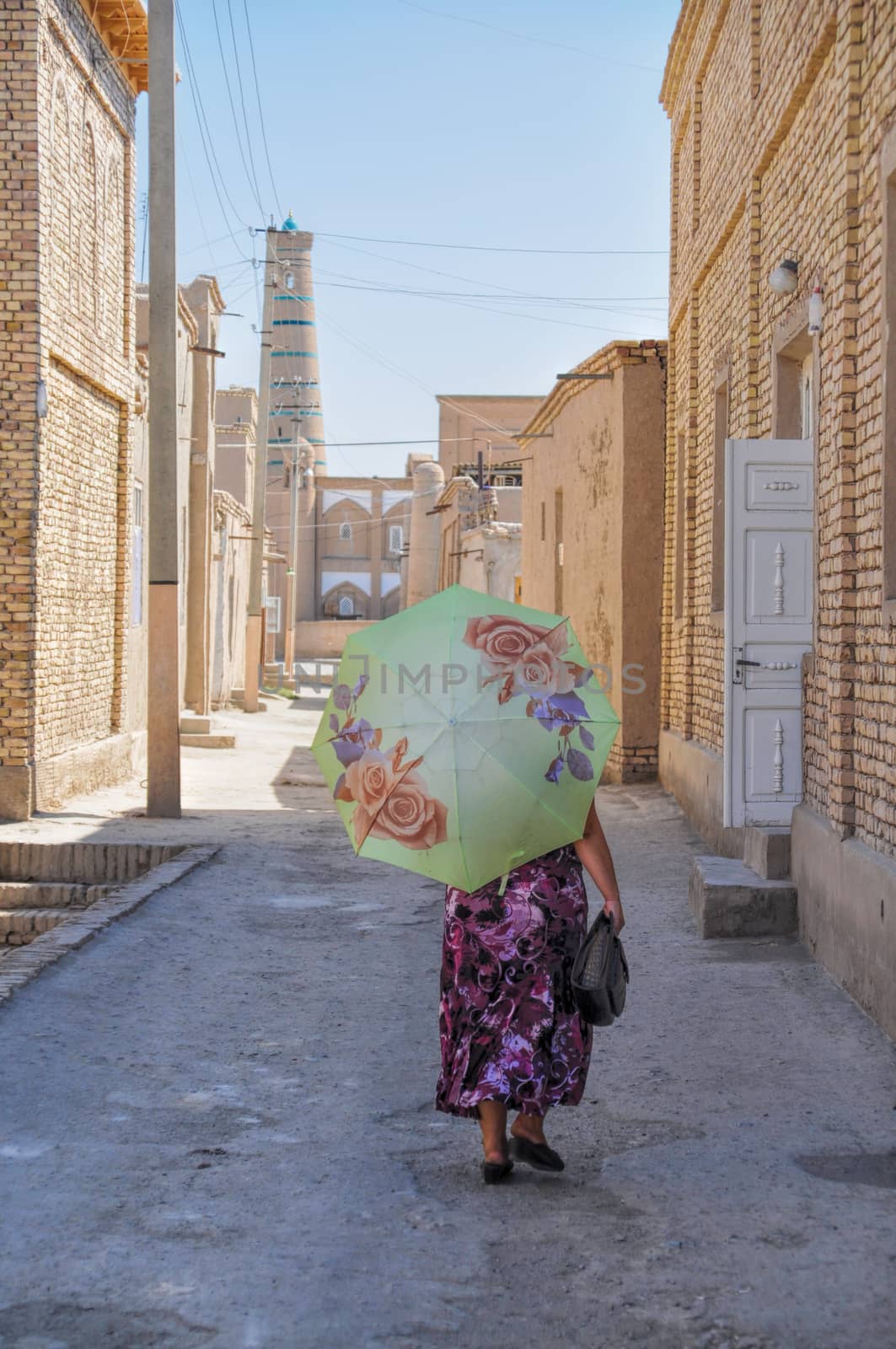 Uzbek woman with parasol walking down the narrow street in Khiva, Uzbekistan