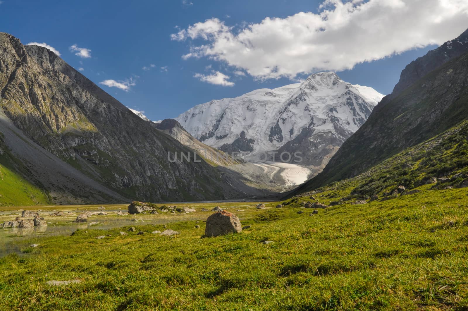 Grassy rocks lying in the valley under snow-covered Tien-Shan Mountains, Kyrgyzstan
