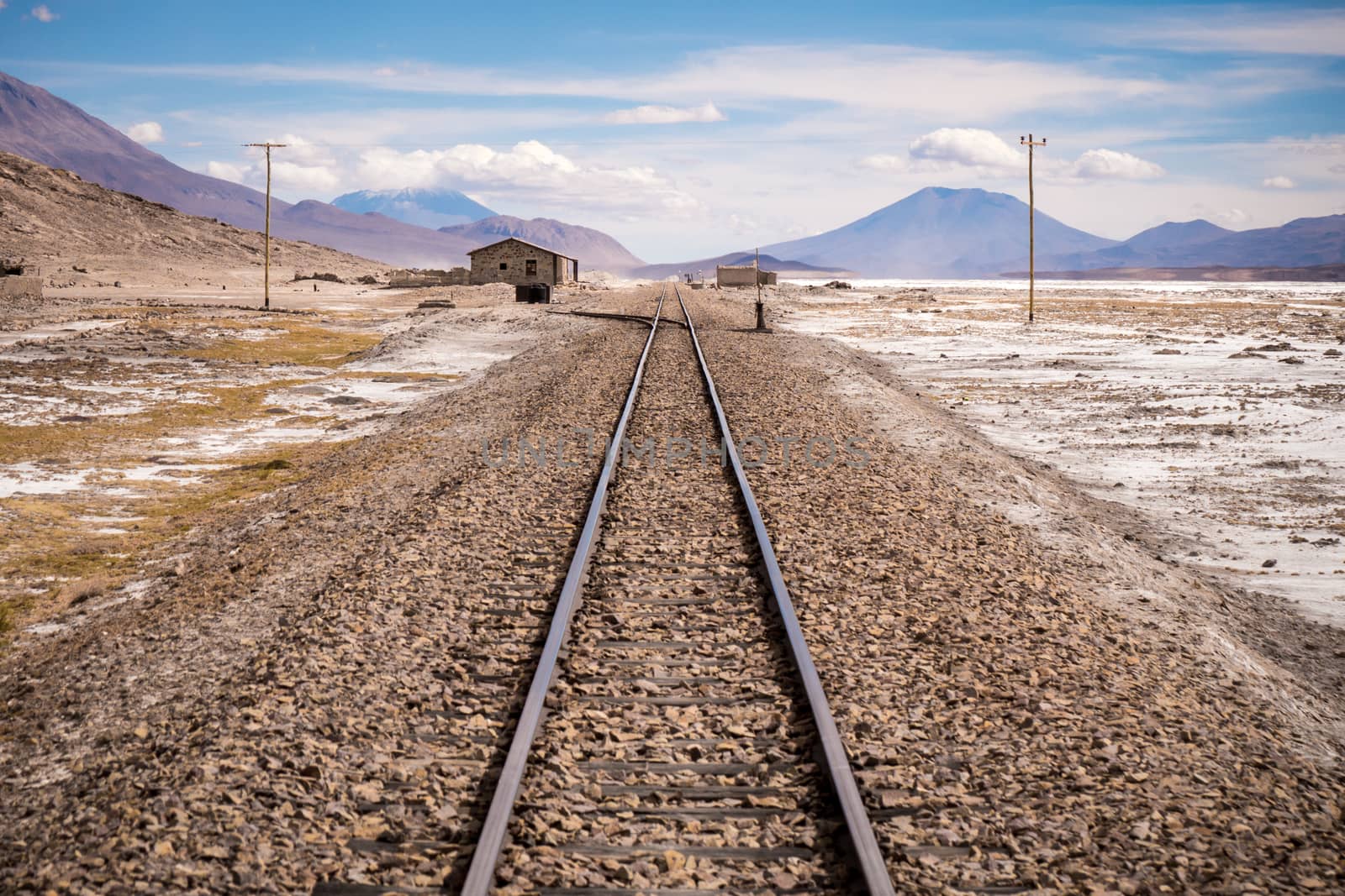 Train tracks passing through a barren, desolate, dry salty earth enviroment then over the horizon into the mountains.