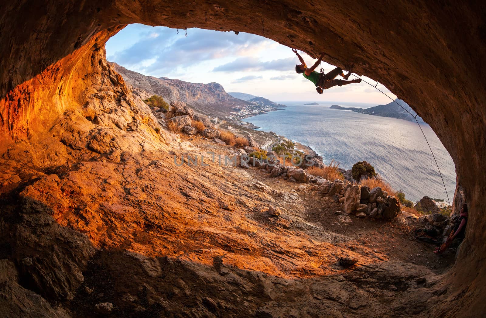 Male rock climber climbing along a roof in a cave by photobac