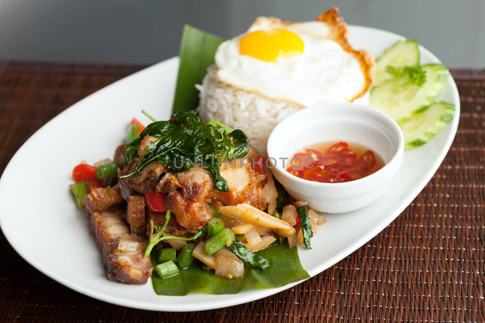Traditional Thai dish crispy pork with a fried egg atop the jasmine rice served with chili sauce.