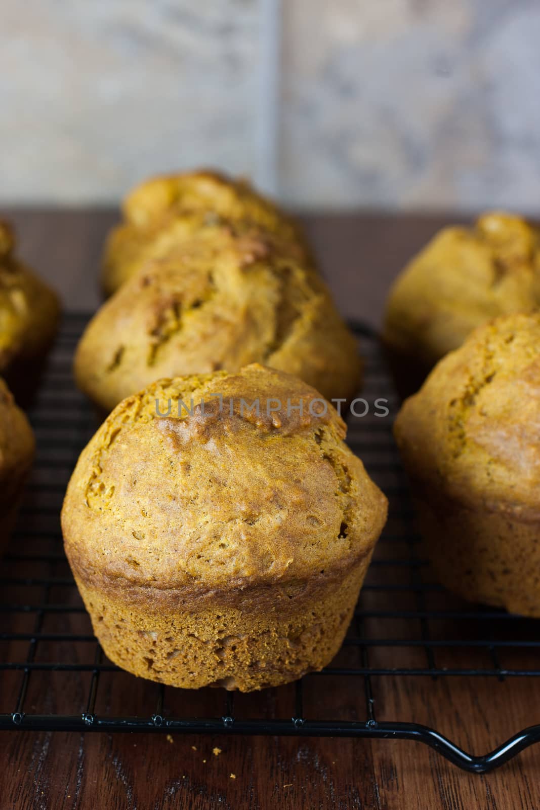 Pumpkin muffins on a metal cooling rack, sitting on a wooden counter.