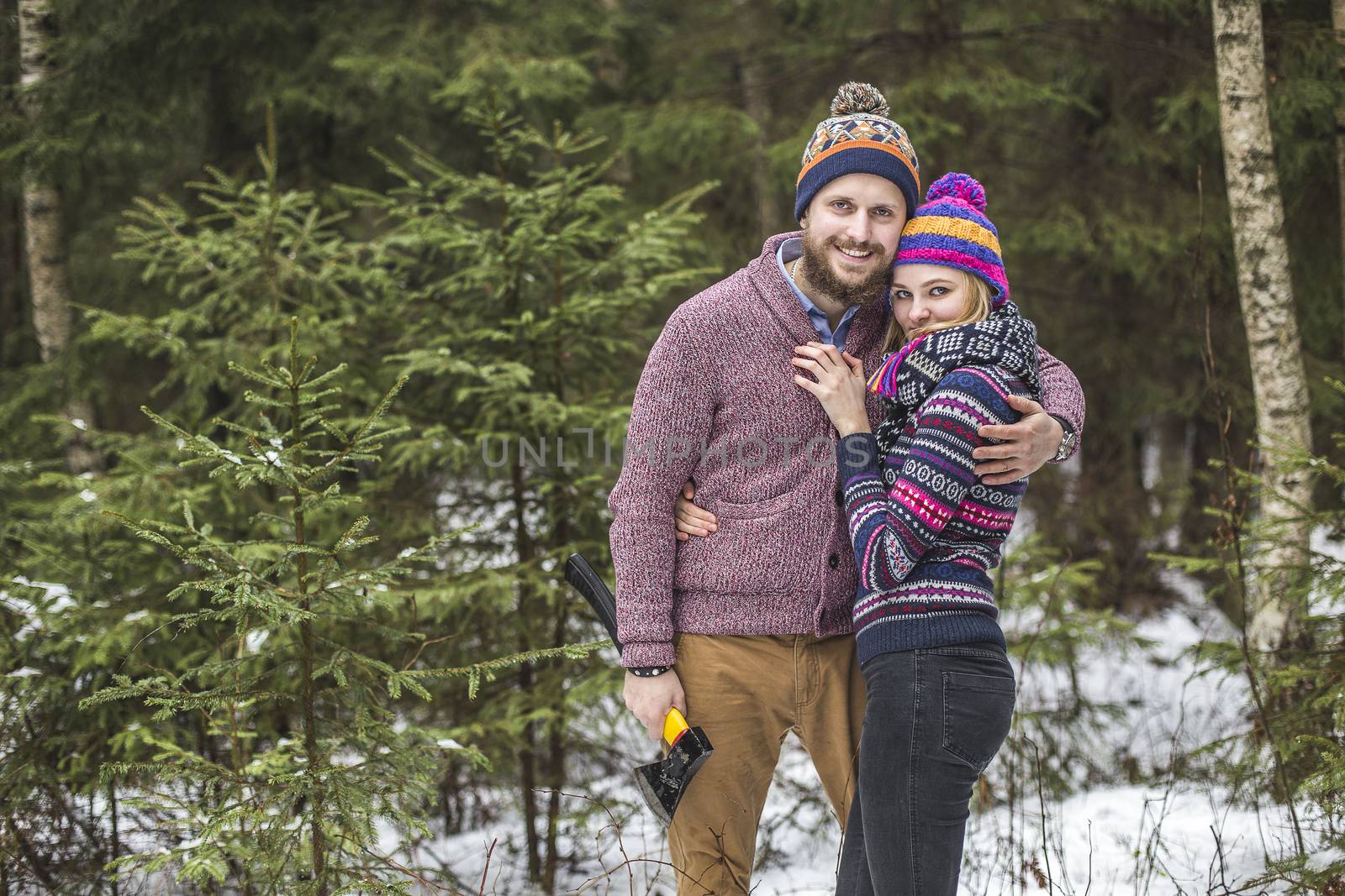 Lovers have a walk in the winter wood with an axe to cut a fir tree