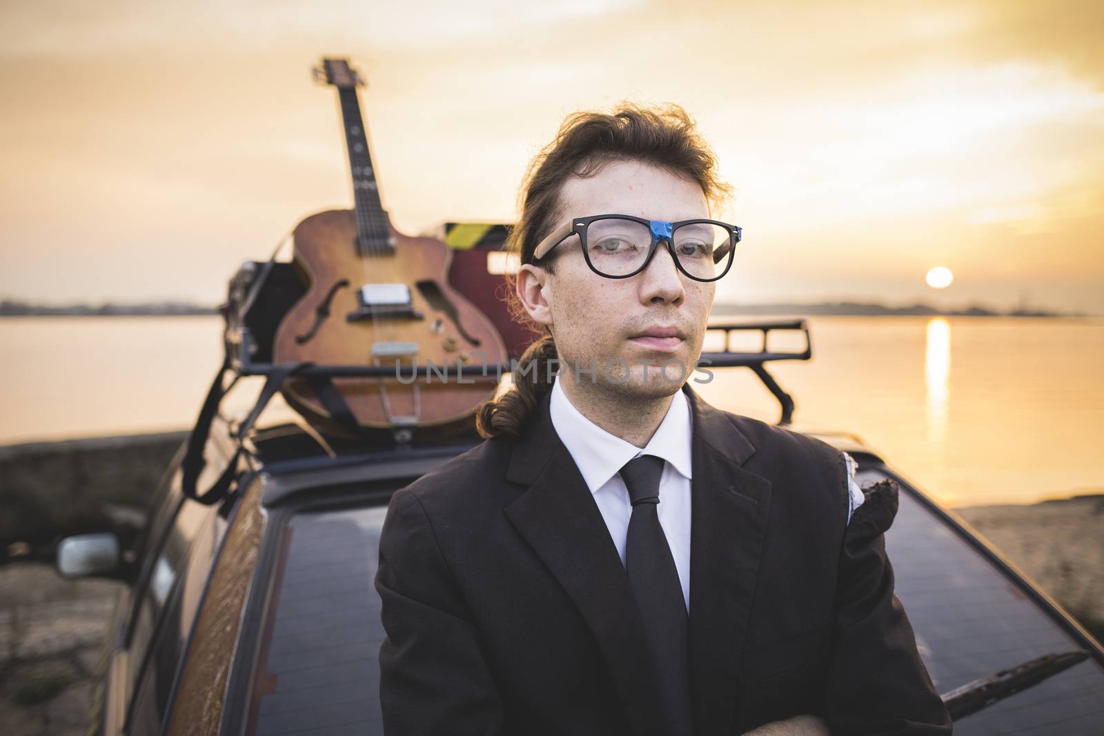 Hipter in glasses and his guitar on car rack by Kor