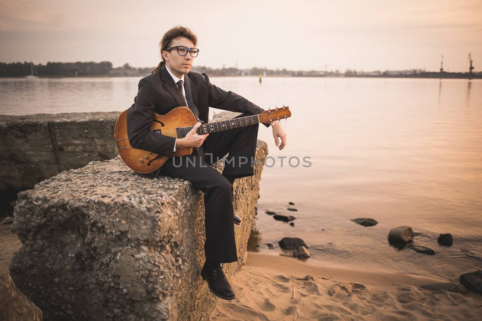 Male musician and his guitar on shore by Kor