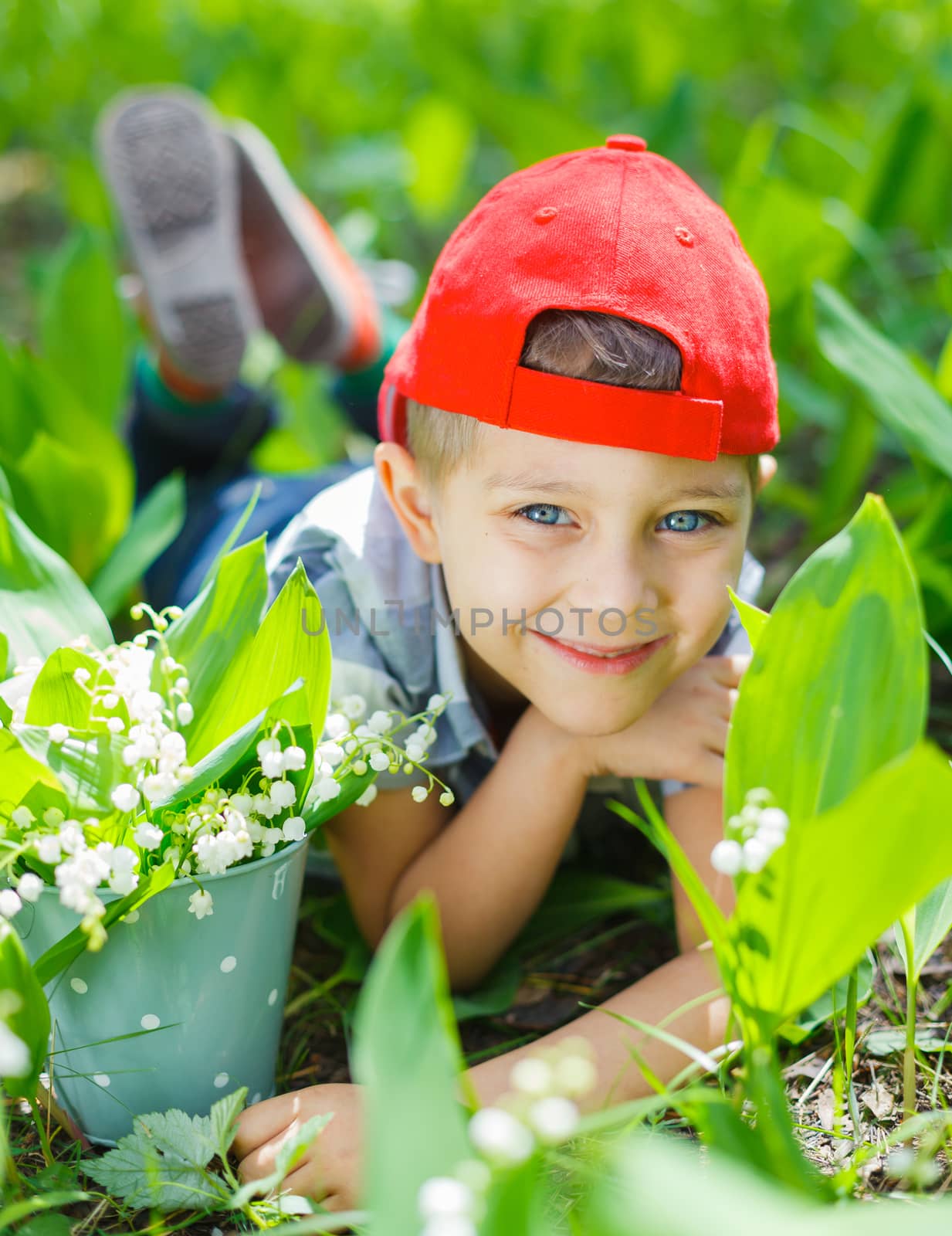 Cute little boy with lilies of the valley in forest on spring day