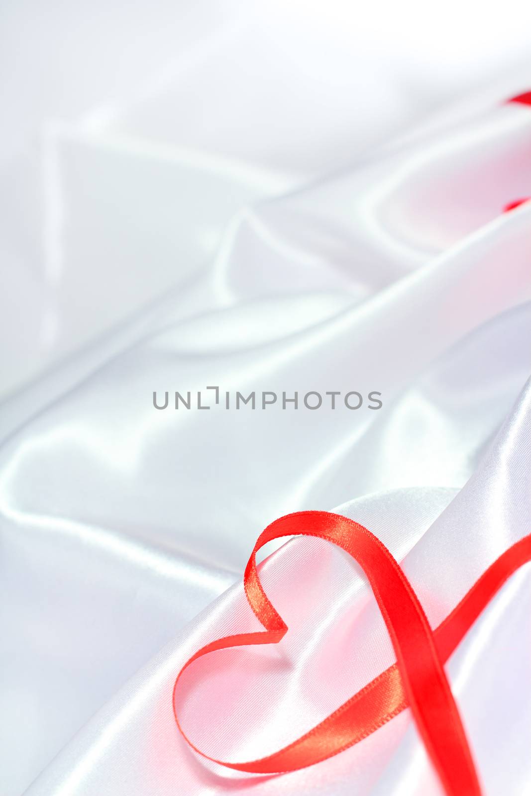 Red satin glossy ribbon heart over white silk background