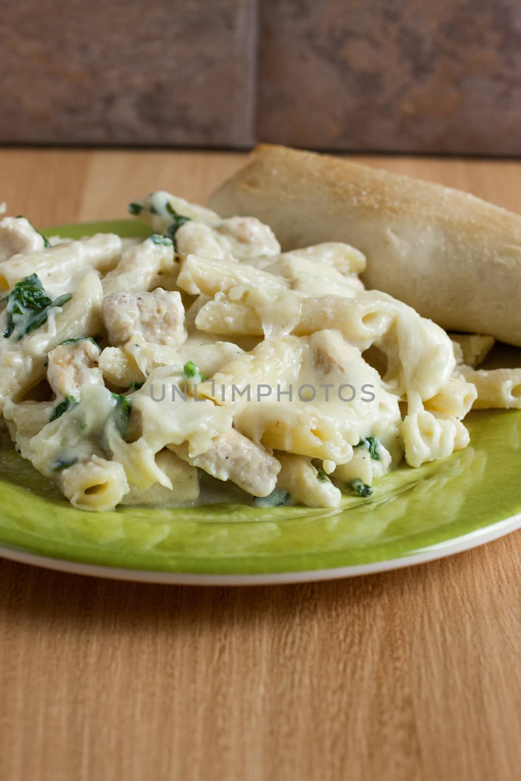 Chicken Florentine pasta with a fresh garlic bread stick opn a green plate.