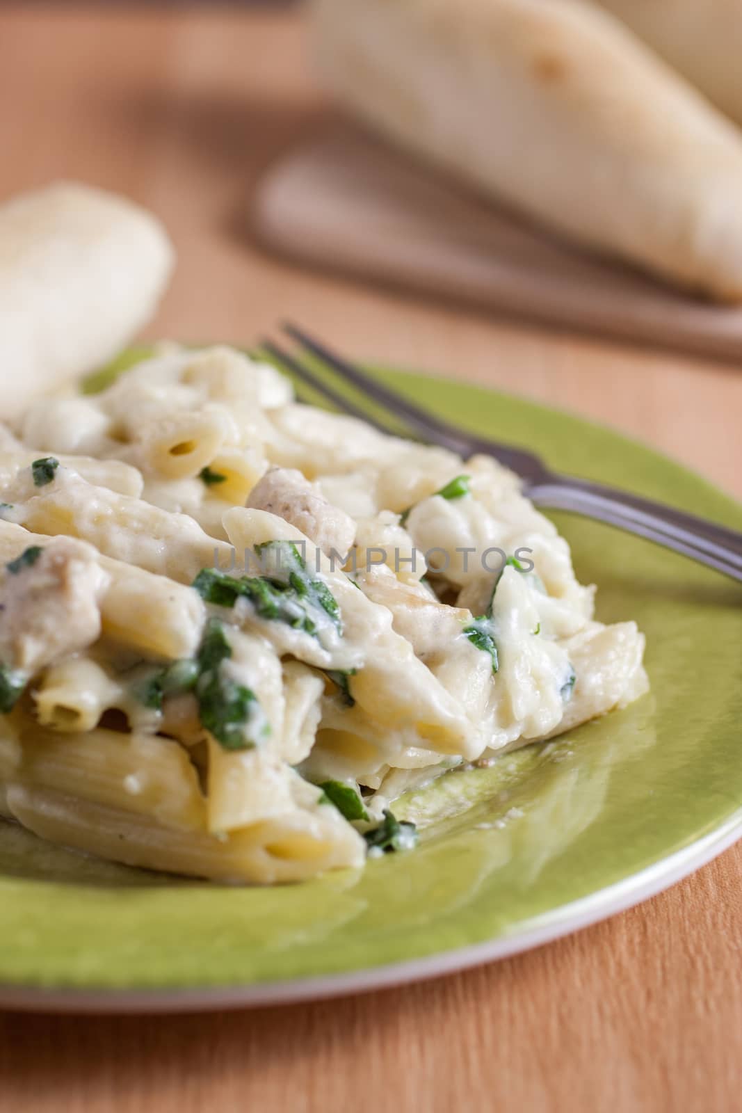 Chicken Florentine pasta with a fresh garlic bread stick opn a green plate.