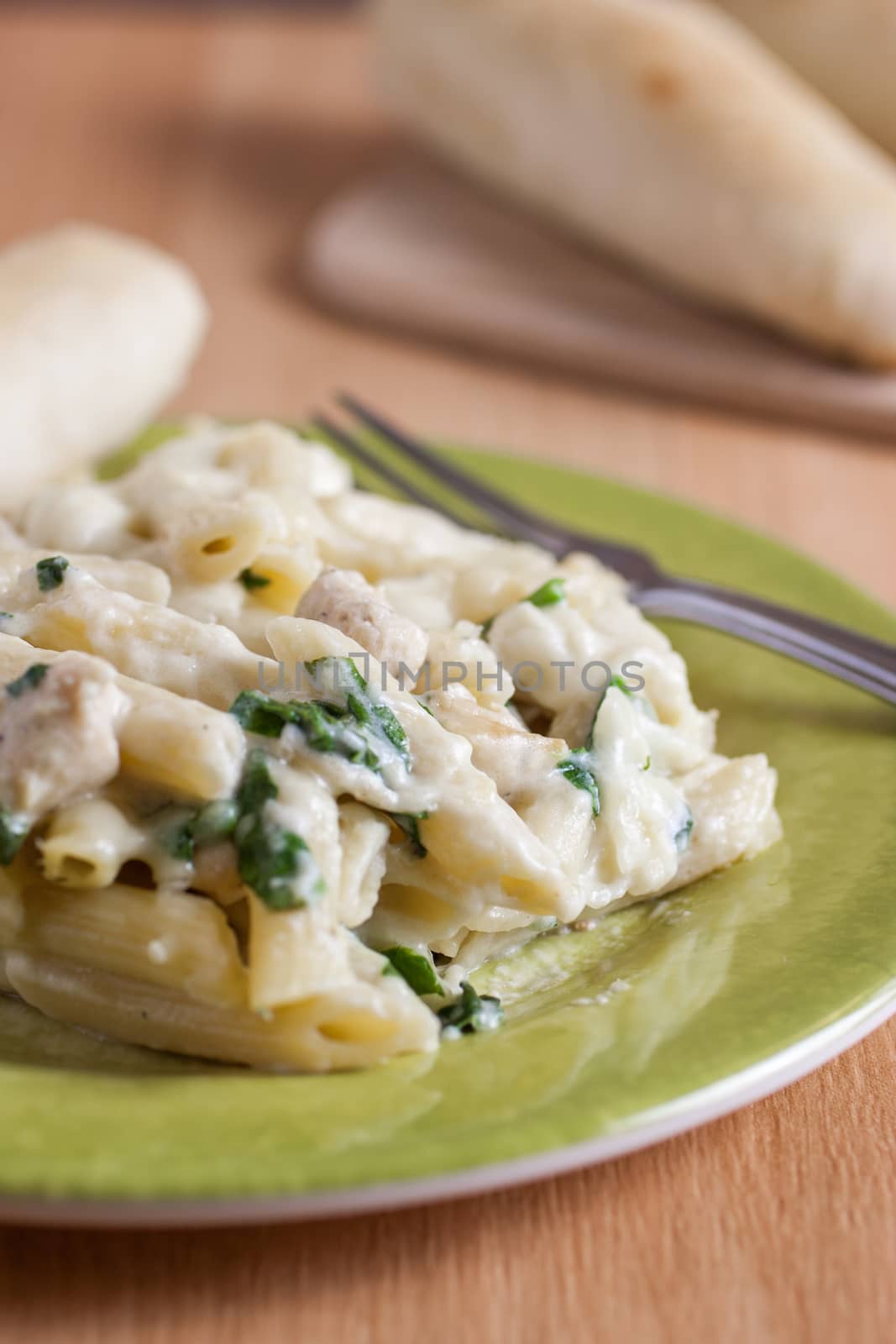 Chicken Florentine pasta with a fresh garlic bread stick opn a green plate.