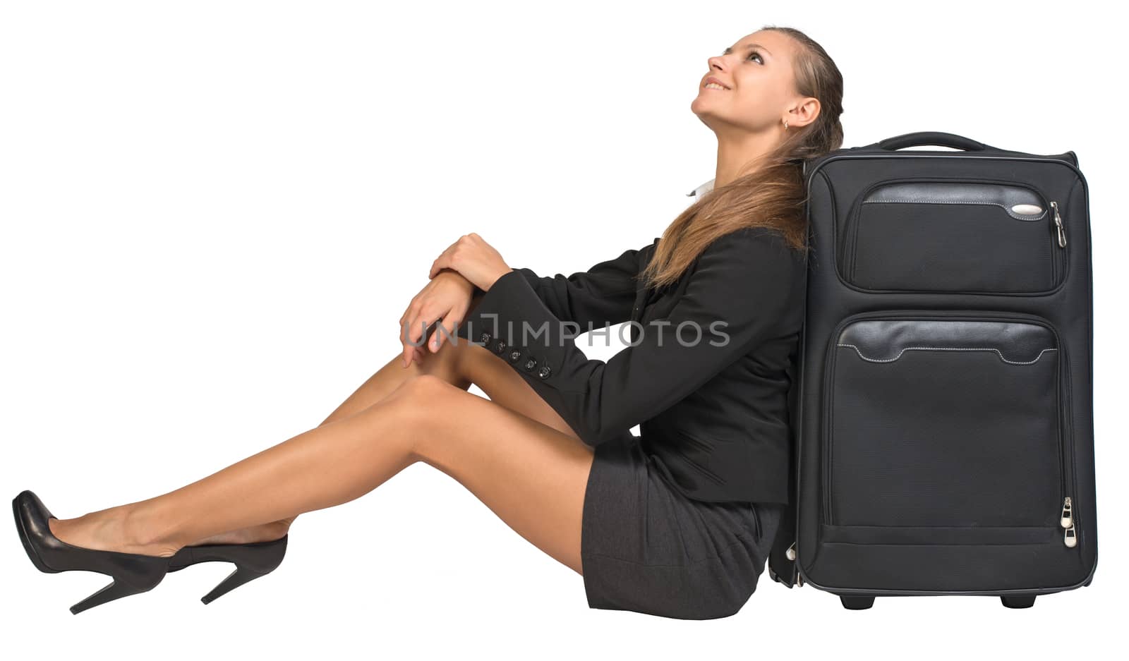 Businesswoman sitting next to front view suitcase, looking upwards, smiling. Isolated over white background