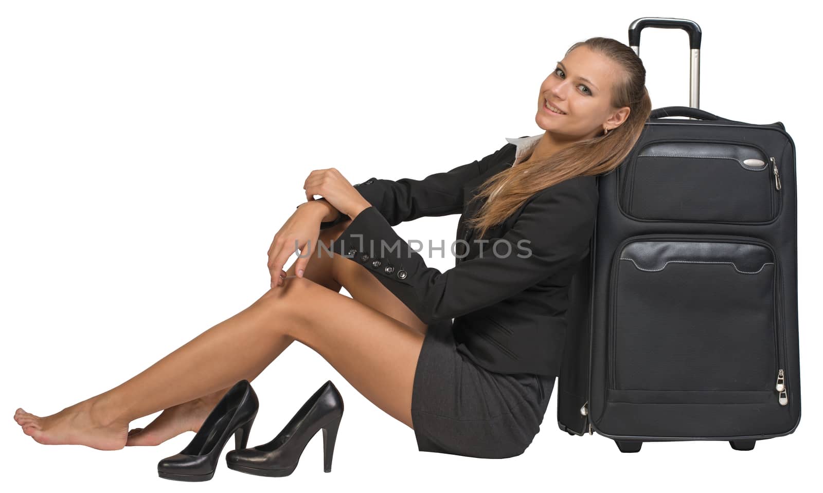 Businesswoman with her shoes off sitting next to front view suitcase with extended handle, looking at camera, smiling. Isolated over white background