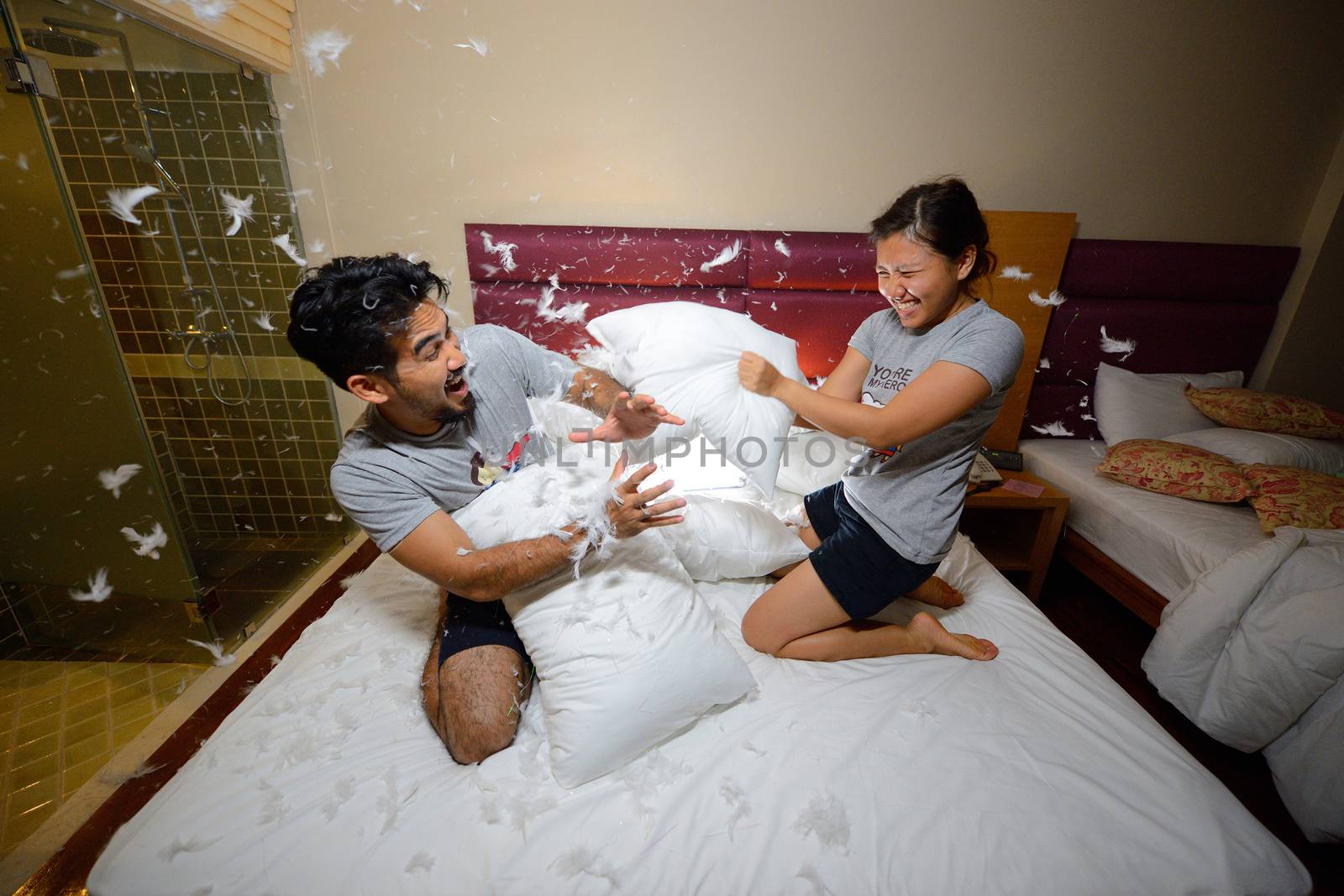 happy loving asian couple having a pillow fight in bed at night