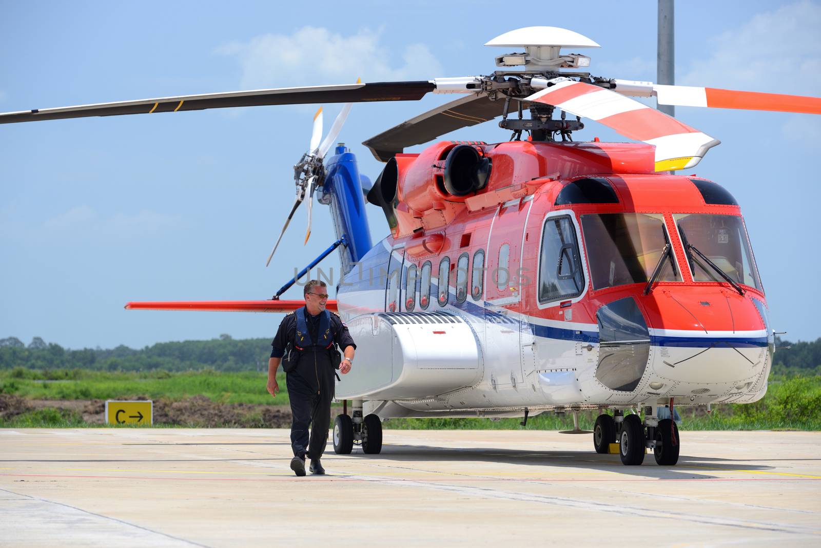 offshore helicopter pilot is walking and smiling beside of S92 helicopter at apron