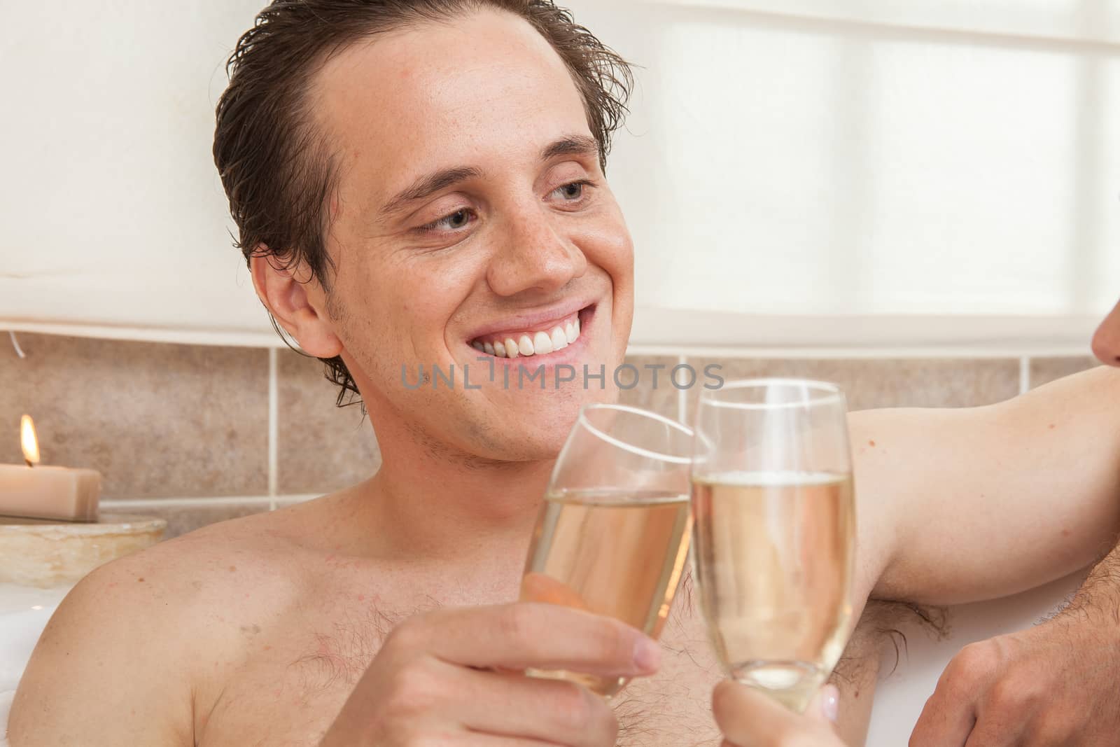 Happy man with champagne toasts in the bathtub