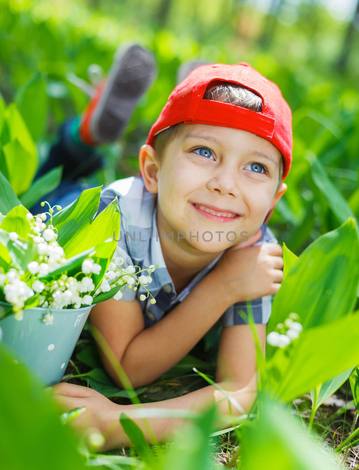 Cute little boy with lilies of the valley in forest on spring day