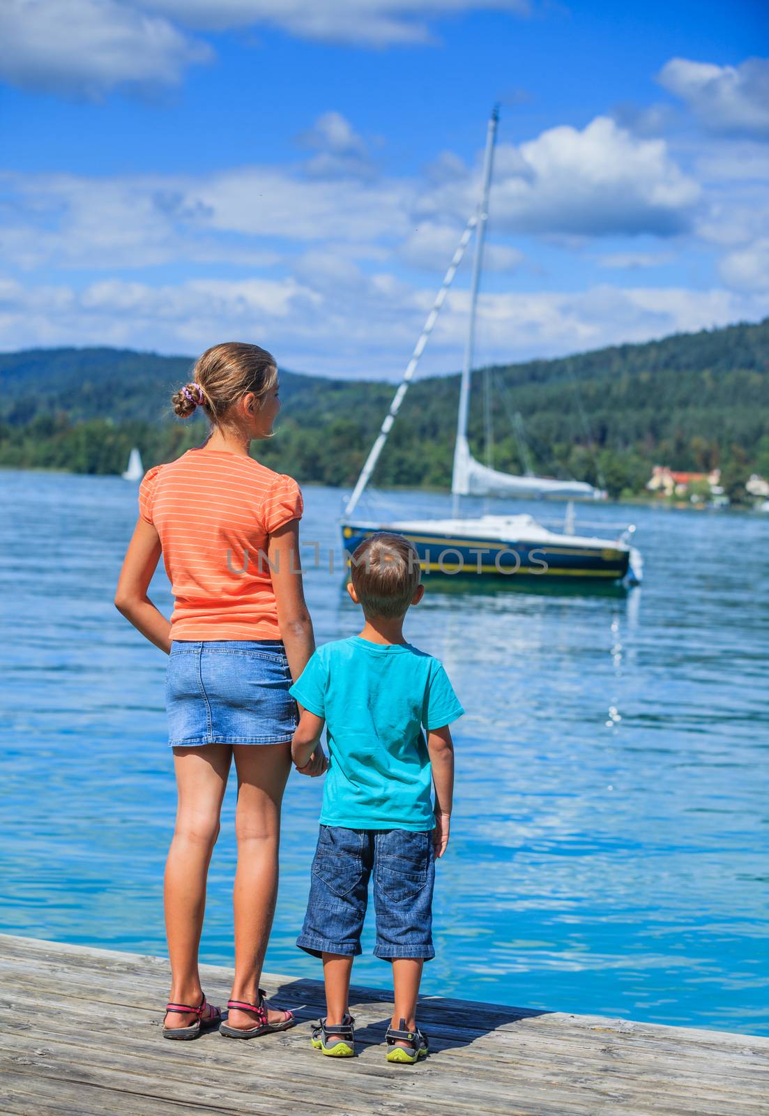 Summer vacation  at the lake - two happy kids walking on the pier and watching on the yacht