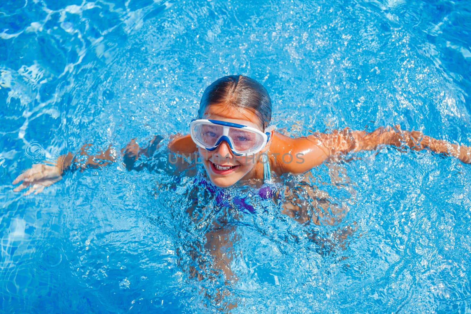 Cute happy young girl in goggles swimming and snorking in the swimming pool