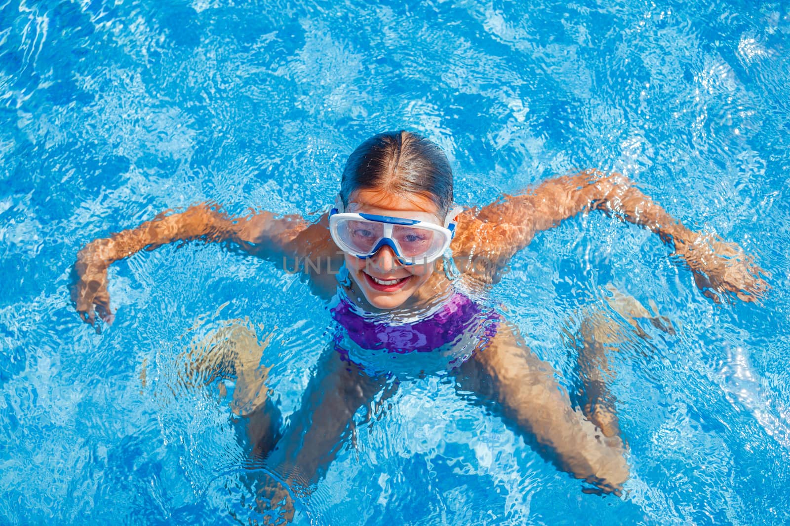 Cute happy young girl in goggles swimming and snorking in the swimming pool