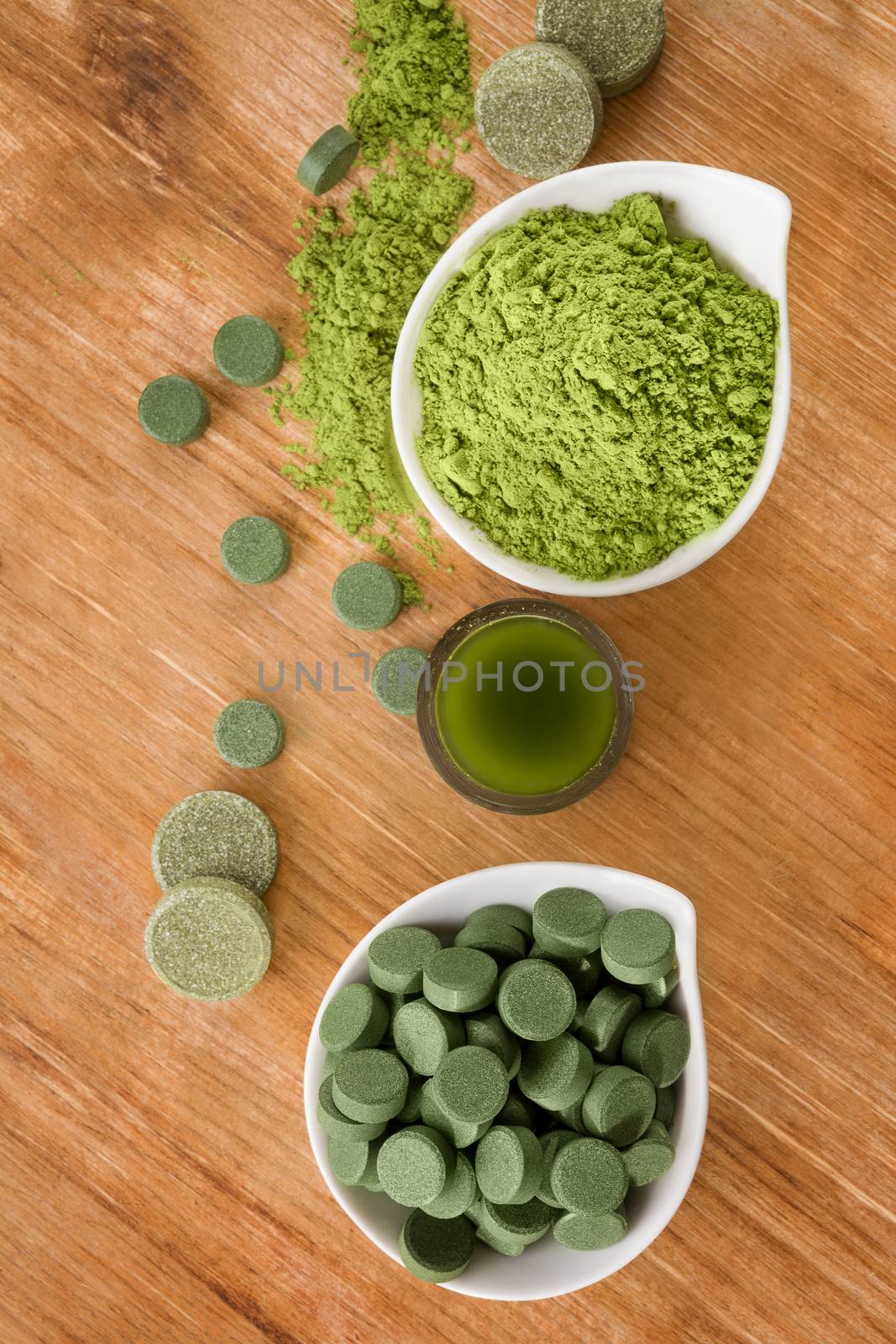 Detox. Chlorella pills, wheat grass powder and green drink in glass on brown wooden background, top view. Natural alternative medicine, weight loss and detox.