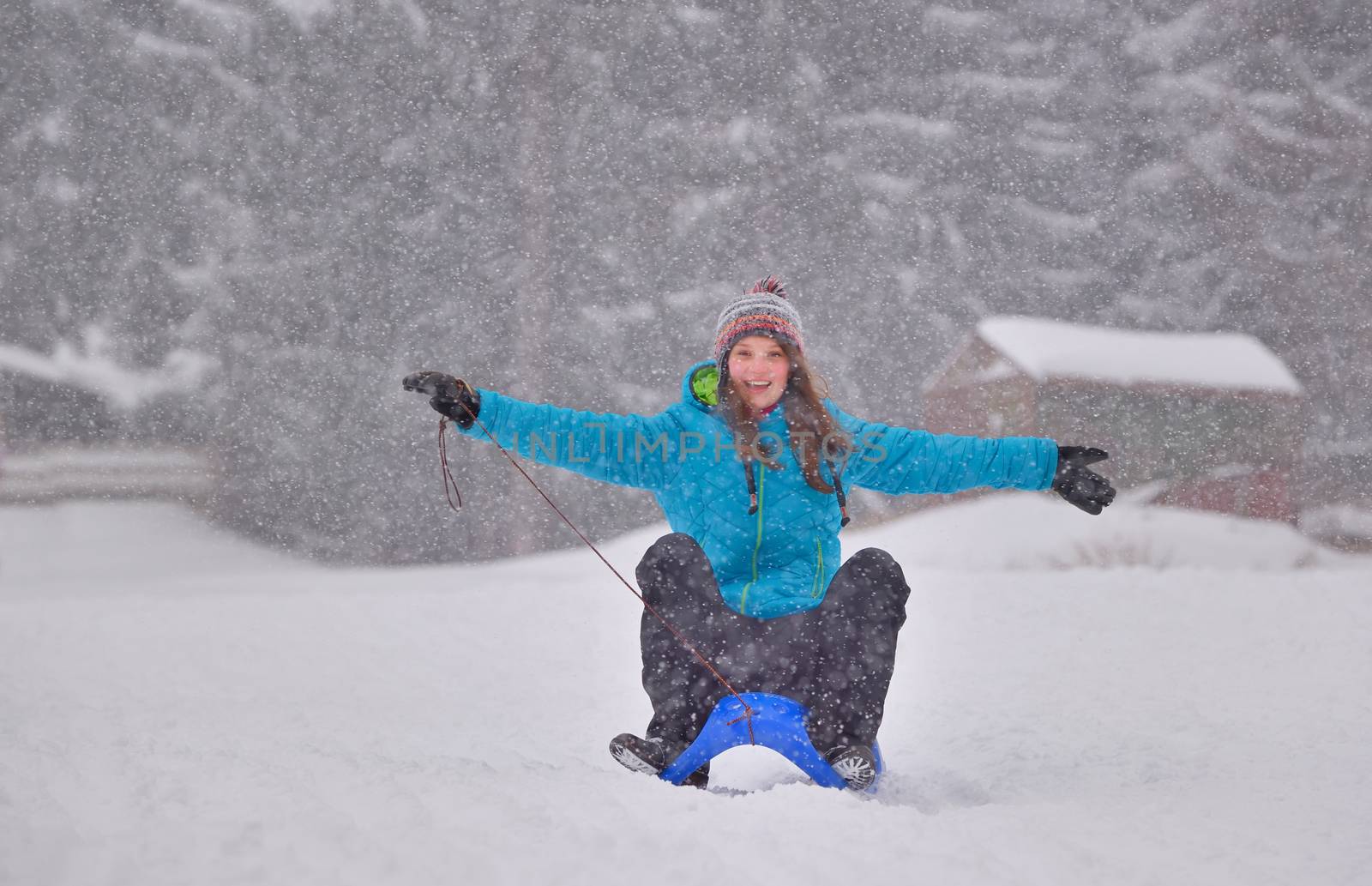 Excited girl sledding on sled while snowing with open arms