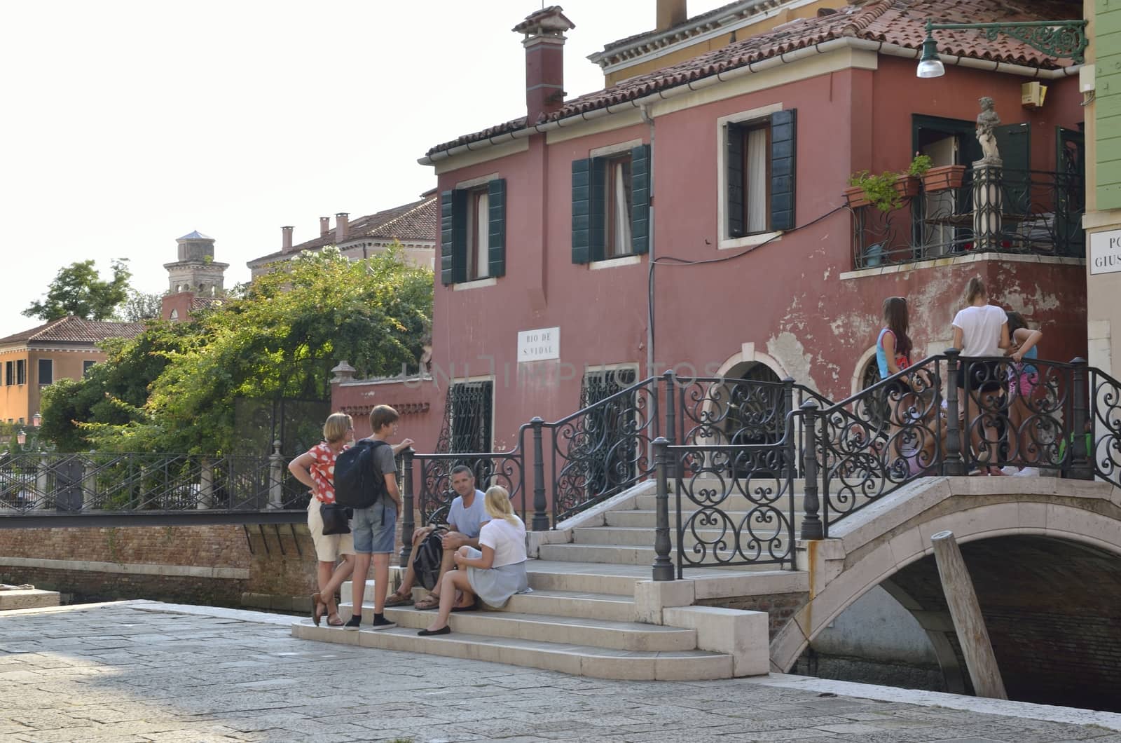Tourists resting on stairs at a bridge in canal of San Vidal in Venice, Italy