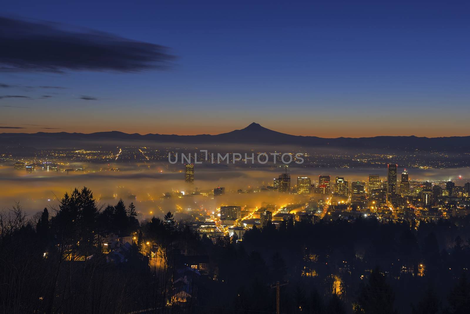 Thick Fog Rolling at Dawn over cityscape of downtown Portland Oregon with city lights and silhouette of Mt Hood