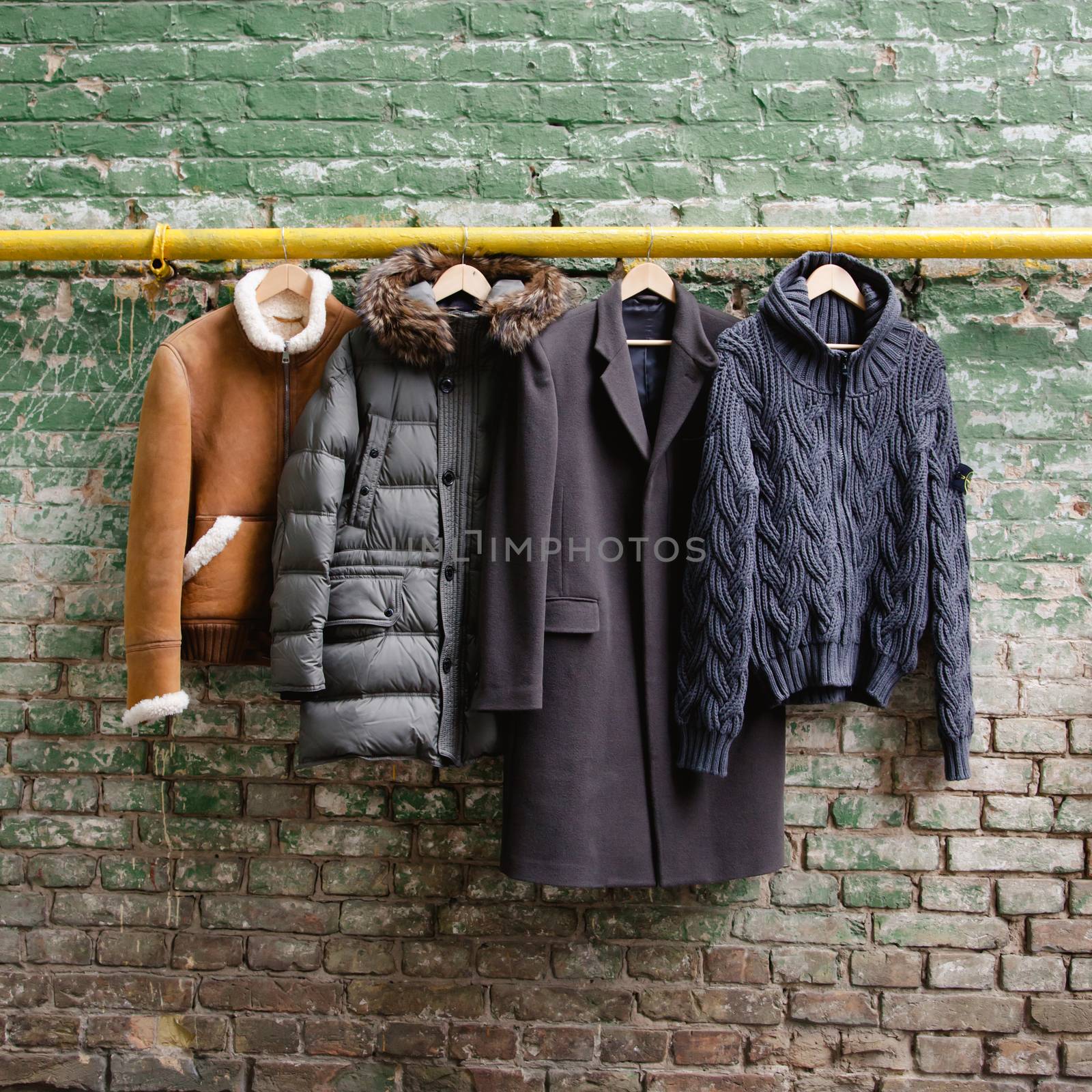 Men's trendy clothing on hangers on grunge brick wall. Concept background