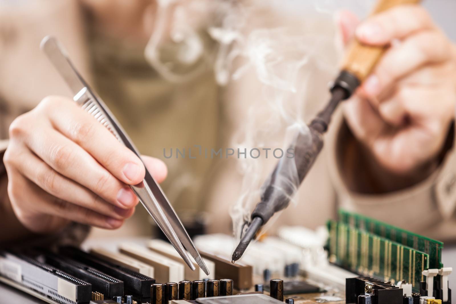 Manual worker human hand holding soldering iron tool repairing computer electronics circuit board