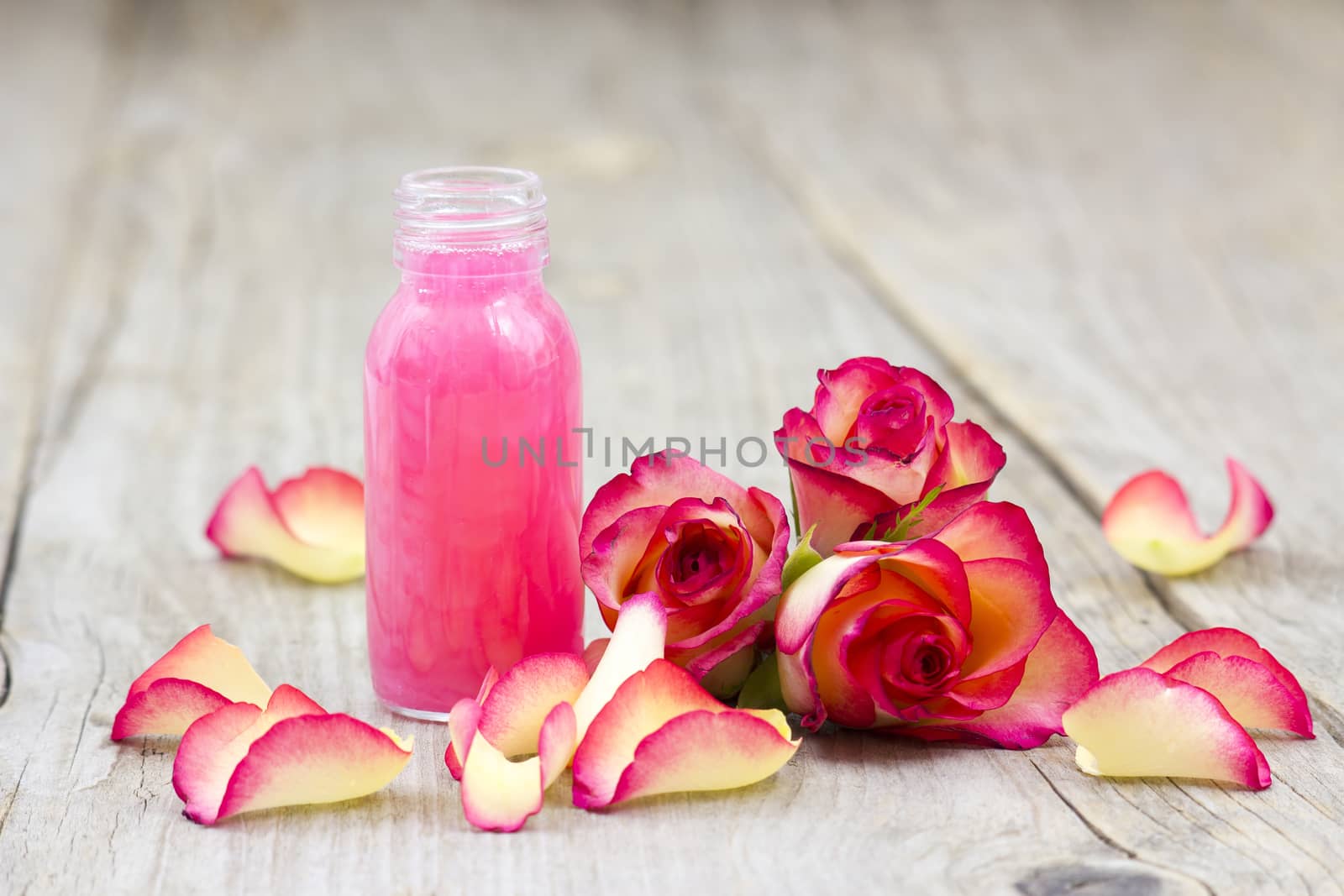 bath oil and pink roses on old wooden background