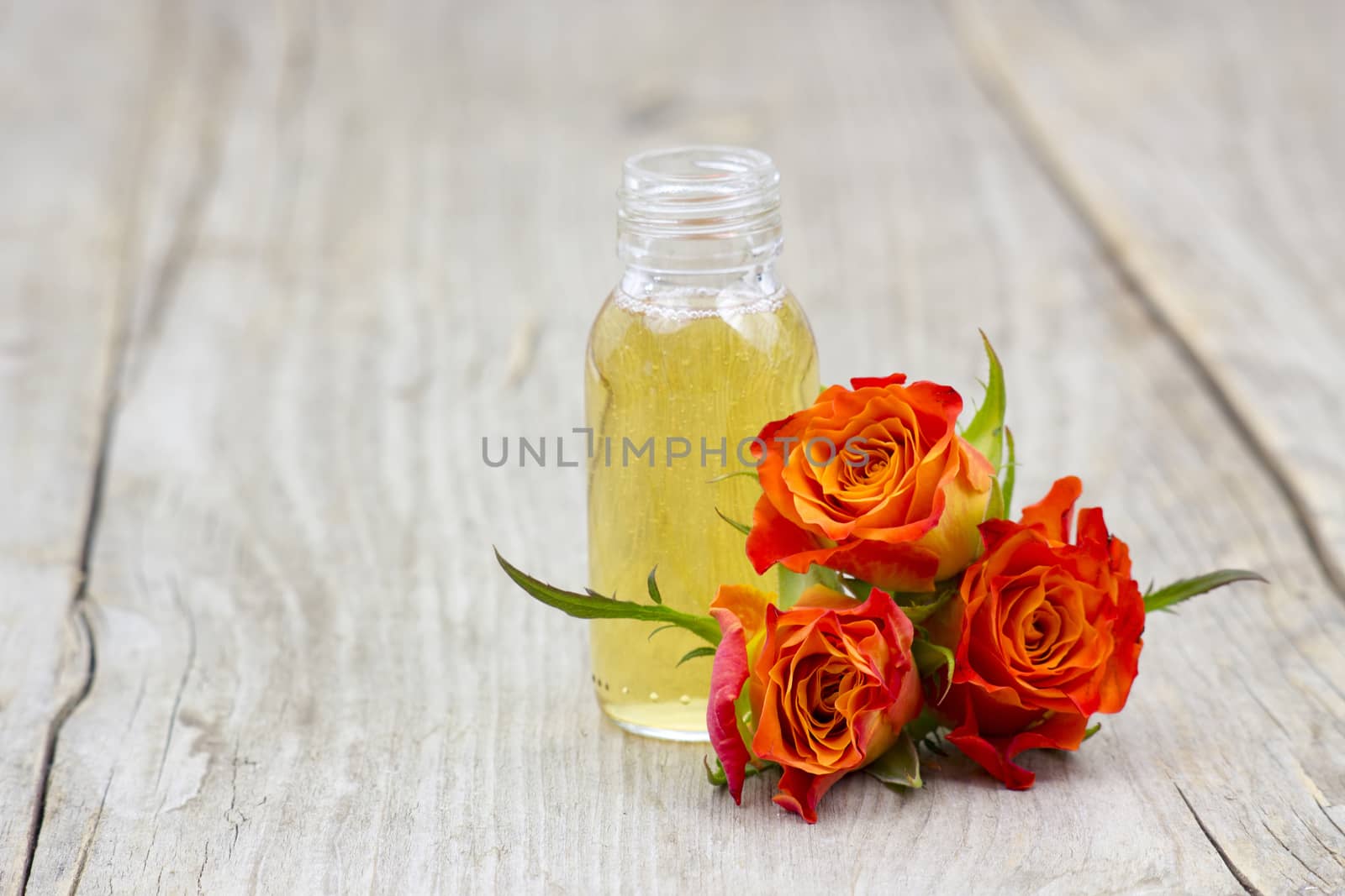 bath oil and orange roses on old wooden background