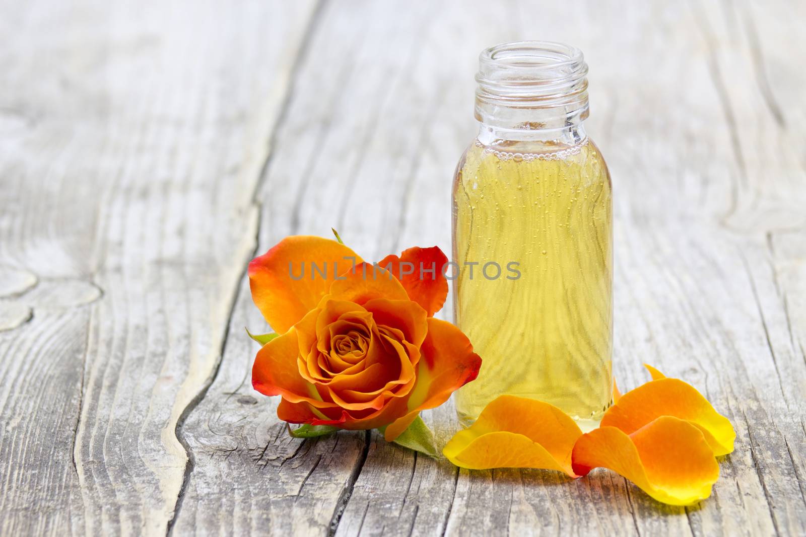 bath oil and orange rose on old wooden background