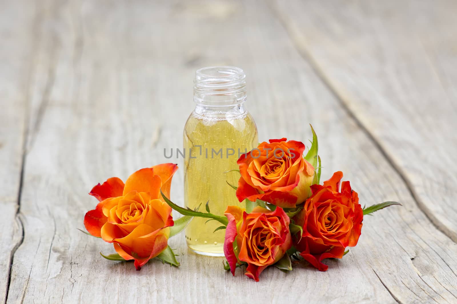 bath oil and orange roses on old wooden background