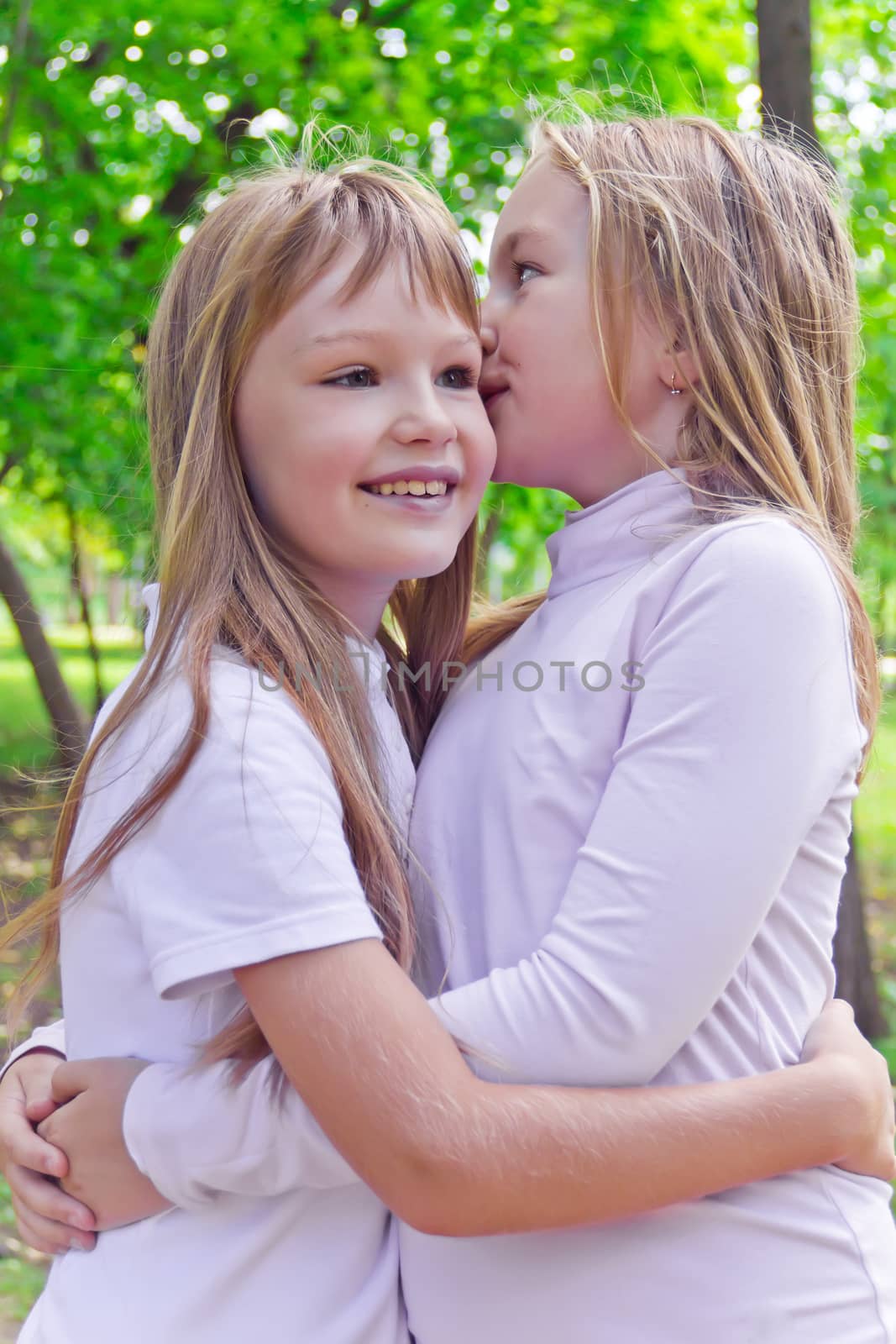 Photo of two smiling whispering girls in summer