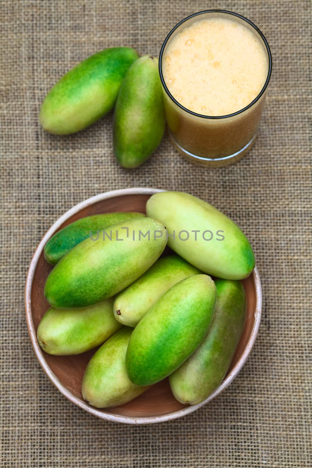 Latin American fruit called banana passionfruit (lat. Passiflora tripartita) (in Spanish mostly tumbo, curuba, taxo) in bowl and banana passionfruit juice in glass (Selective Focus, Focus on the upper fruits in the bowl and the top of the juice)