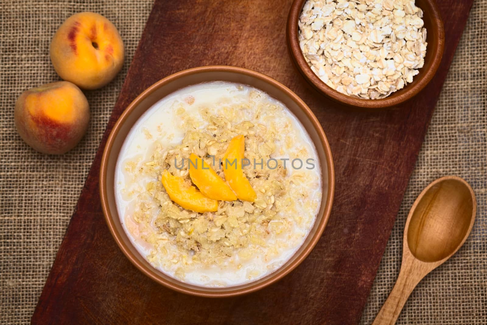 Bowl of oatmeal porridge served with peach slices photographed with natural light (Selective Focus, Focus on the top of the meal)