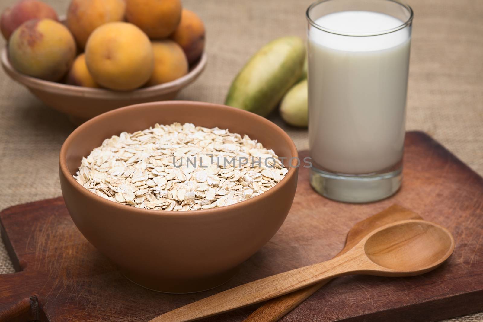 Bowl full of rolled oats with a glass of milk and peaches in the back photographed with natural light (Selective Focus, Focus on the oats in the front)